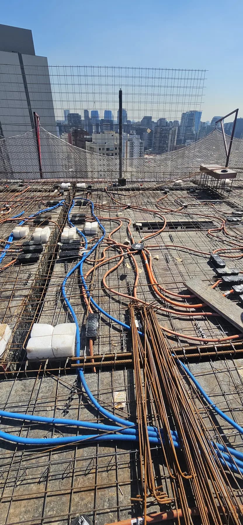 Vista da laje de edifício com eletrodutos laranja para energia e azuis para comunicação passando pela armação